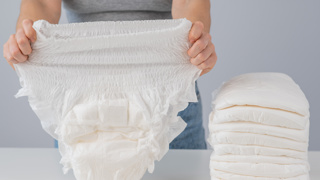 Person holding up an adult incontinence pant with a stack beside them – incontinence pants offer elderly parents discreet, comfortable protection against leaks, helping maintain dignity and hygiene throughout the day.