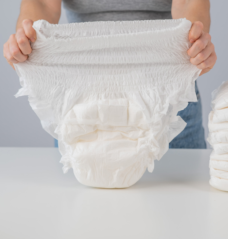 Person holding up an adult incontinence pant with a stack beside them – incontinence pants offer elderly parents discreet, comfortable protection against leaks, helping maintain dignity and hygiene throughout the day.