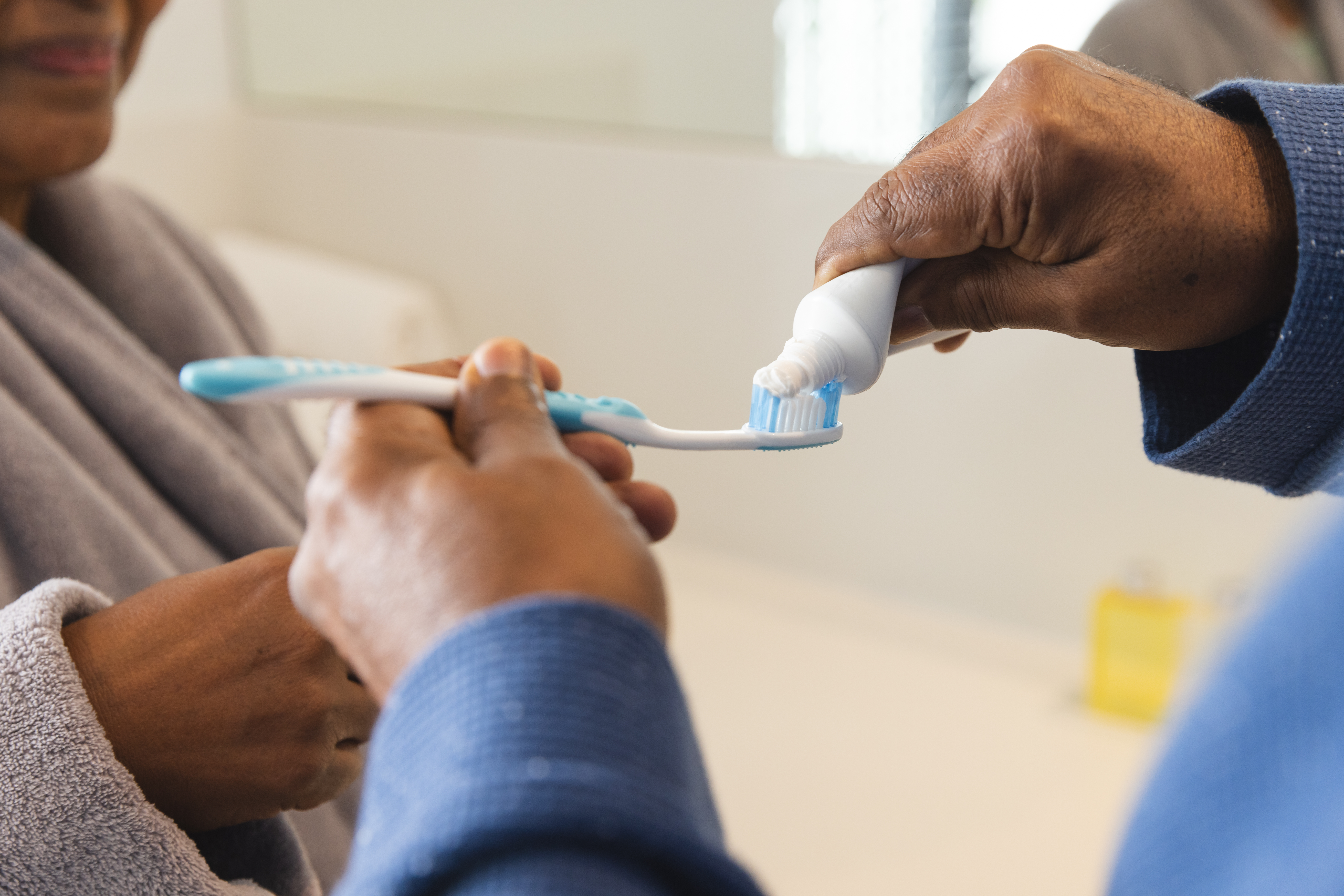 Carer helping to apply toothpaste onto a toothbrush – ergonomic toothbrushes with soft bristles are ideal for elderly parents with reduced dexterity or sensitive gums to maintain good oral hygiene.