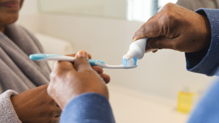 Carer helping to apply toothpaste onto a toothbrush – ergonomic toothbrushes with soft bristles are ideal for elderly parents with reduced dexterity or sensitive gums to maintain good oral hygiene.
