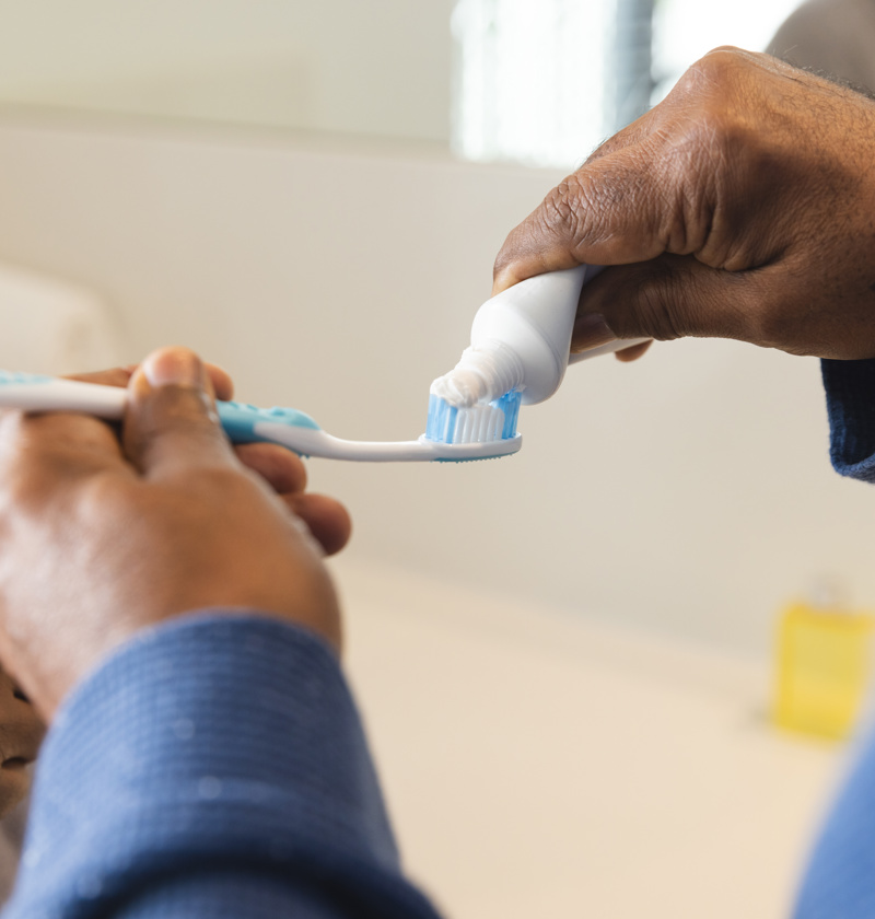 Carer helping to apply toothpaste onto a toothbrush – ergonomic toothbrushes with soft bristles are ideal for elderly parents with reduced dexterity or sensitive gums to maintain good oral hygiene.