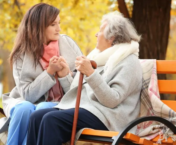 A carent and their elderly parent sitting together on a bench