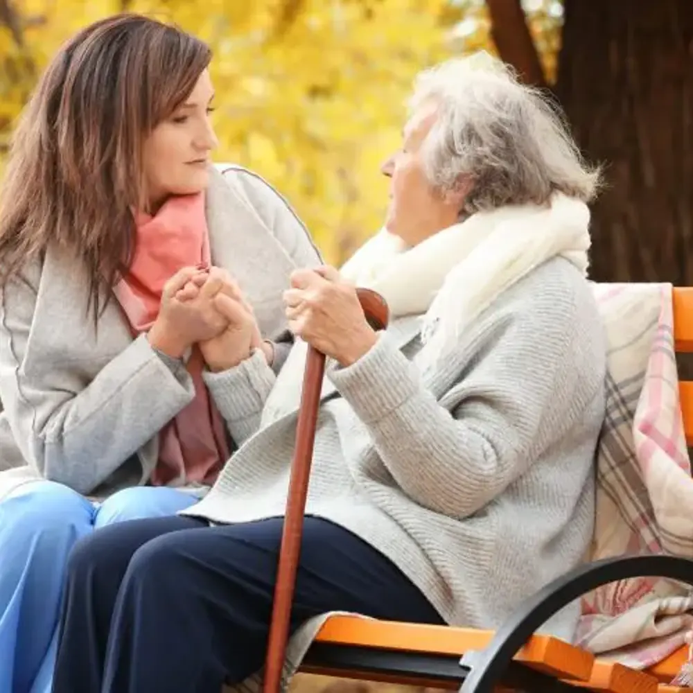 A carent and their elderly parent sitting together on a bench