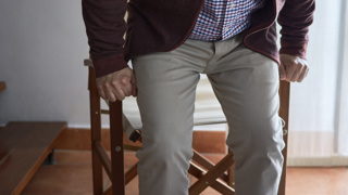 Older adult standing up from a chair, hands gripping the armrests for support – a common scenario for using fall sensor pads to detect instability and help prevent accidents at home.