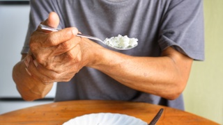 Older adult eating with support from their other hand – highlighting the need for adaptive cutlery designed to help elderly parents with limited grip, arthritis, or hand tremors eat more easily and independently.
