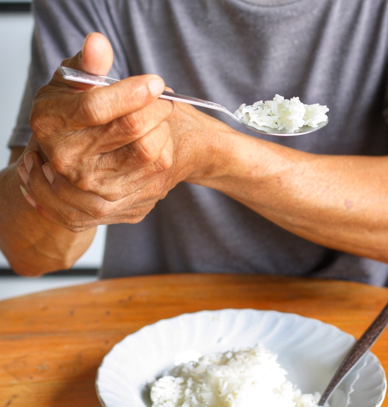 Older adult eating with support from their other hand – highlighting the need for adaptive cutlery designed to help elderly parents with limited grip, arthritis, or hand tremors eat more easily and independently.