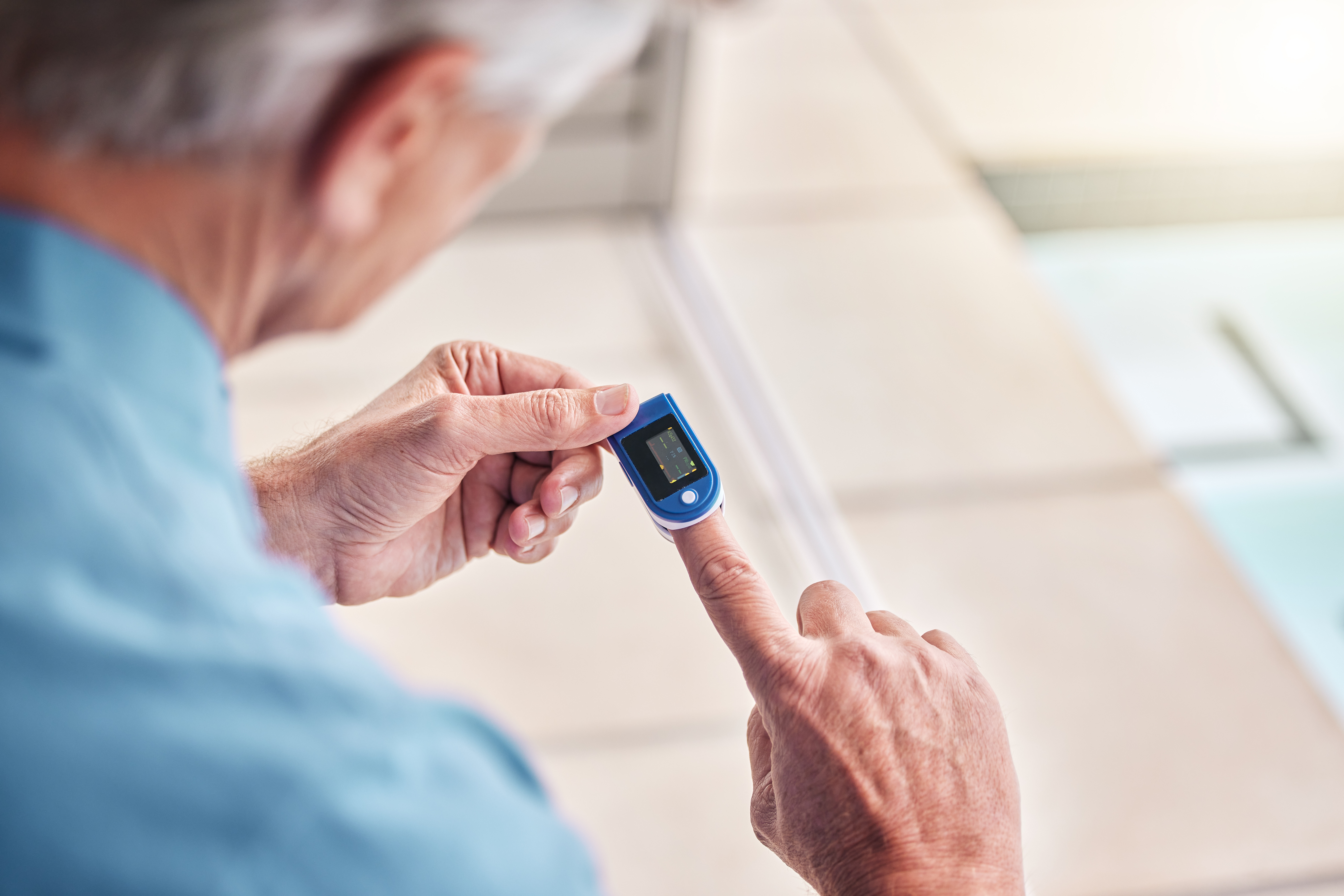 Older adult using a fingertip heart rate and oxygen monitor at home – a simple, portable device ideal for carers tracking vital signs of elderly parents.