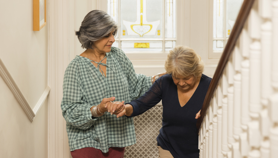 Image of a carent helping their elderly parent up the stairs, but who is looking after their health?