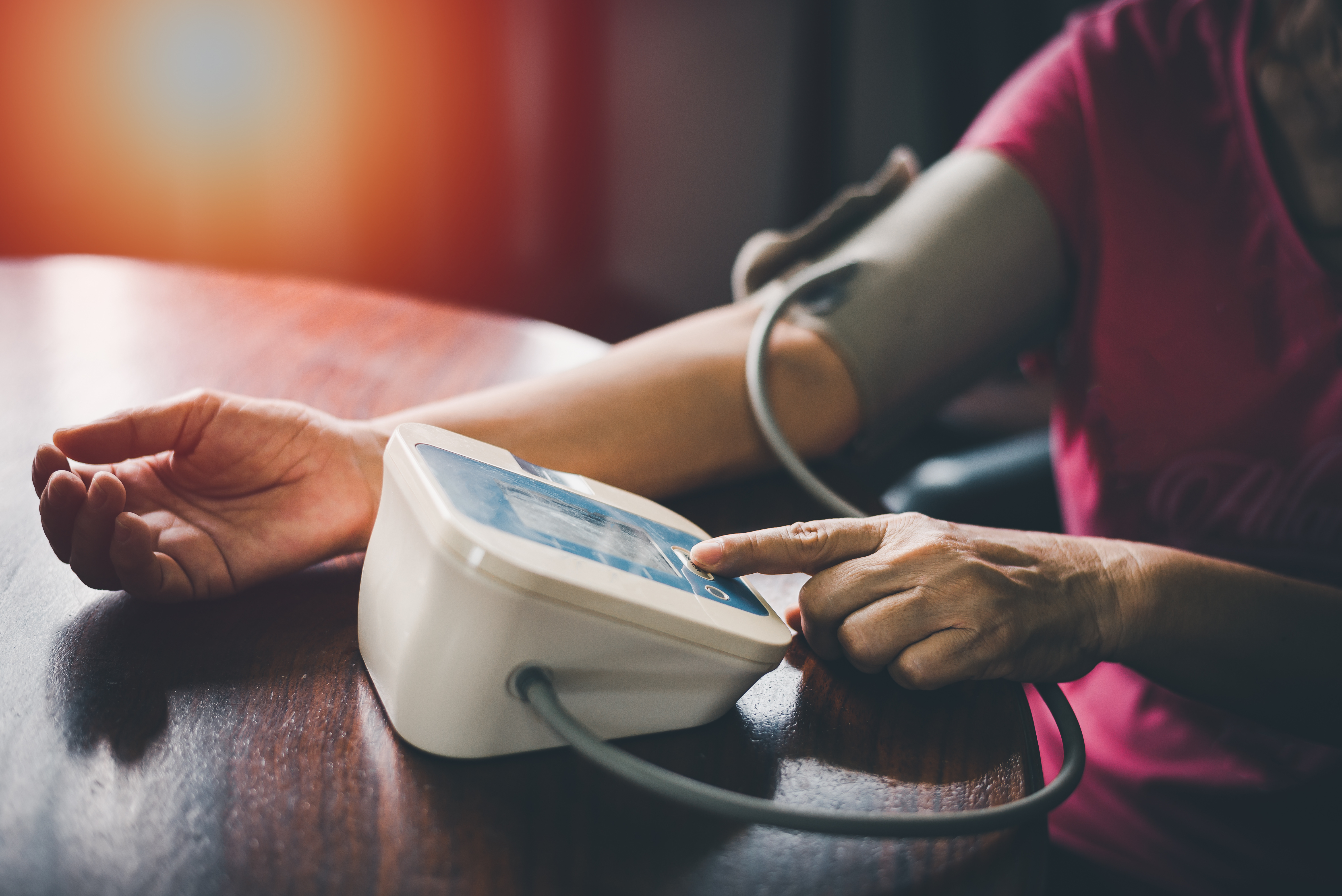 Person using an automatic digital blood pressure monitor at home – an essential health device for carers supporting elderly parents with regular blood pressure checks.