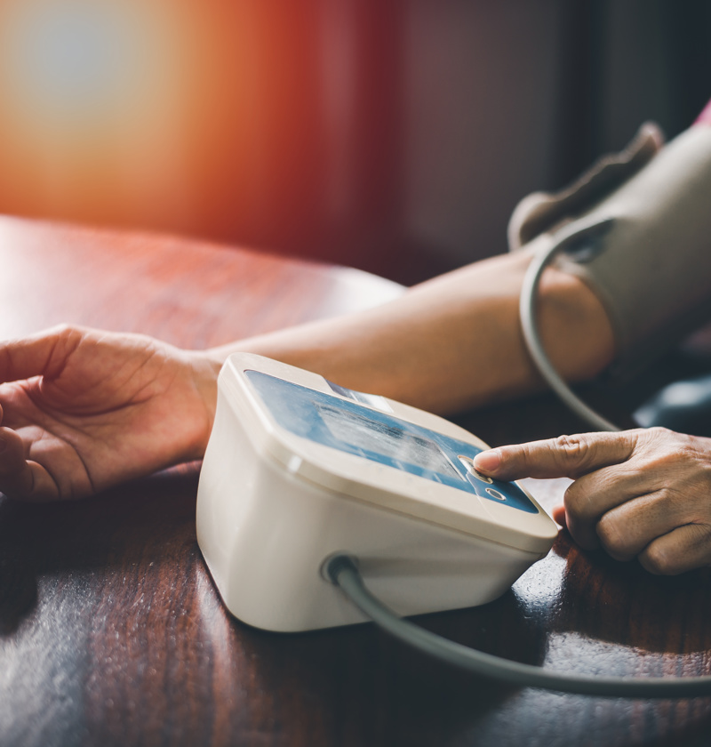 Person using an automatic digital blood pressure monitor at home – an essential health device for carers supporting elderly parents with regular blood pressure checks.