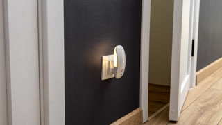 Plug-in motion sensor night light switched on in a hallway – helps elderly parents move safely around the home at night by automatically lighting dark areas without needing to search for switches.