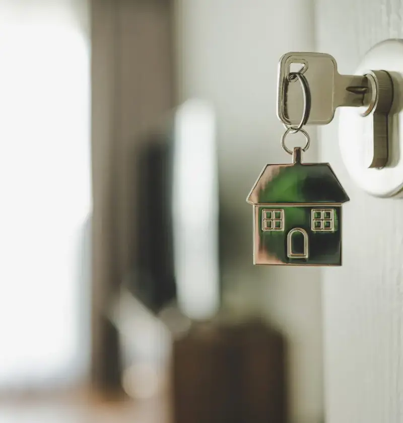 A Key in a lock into a bright home, attached is a keychain of a house