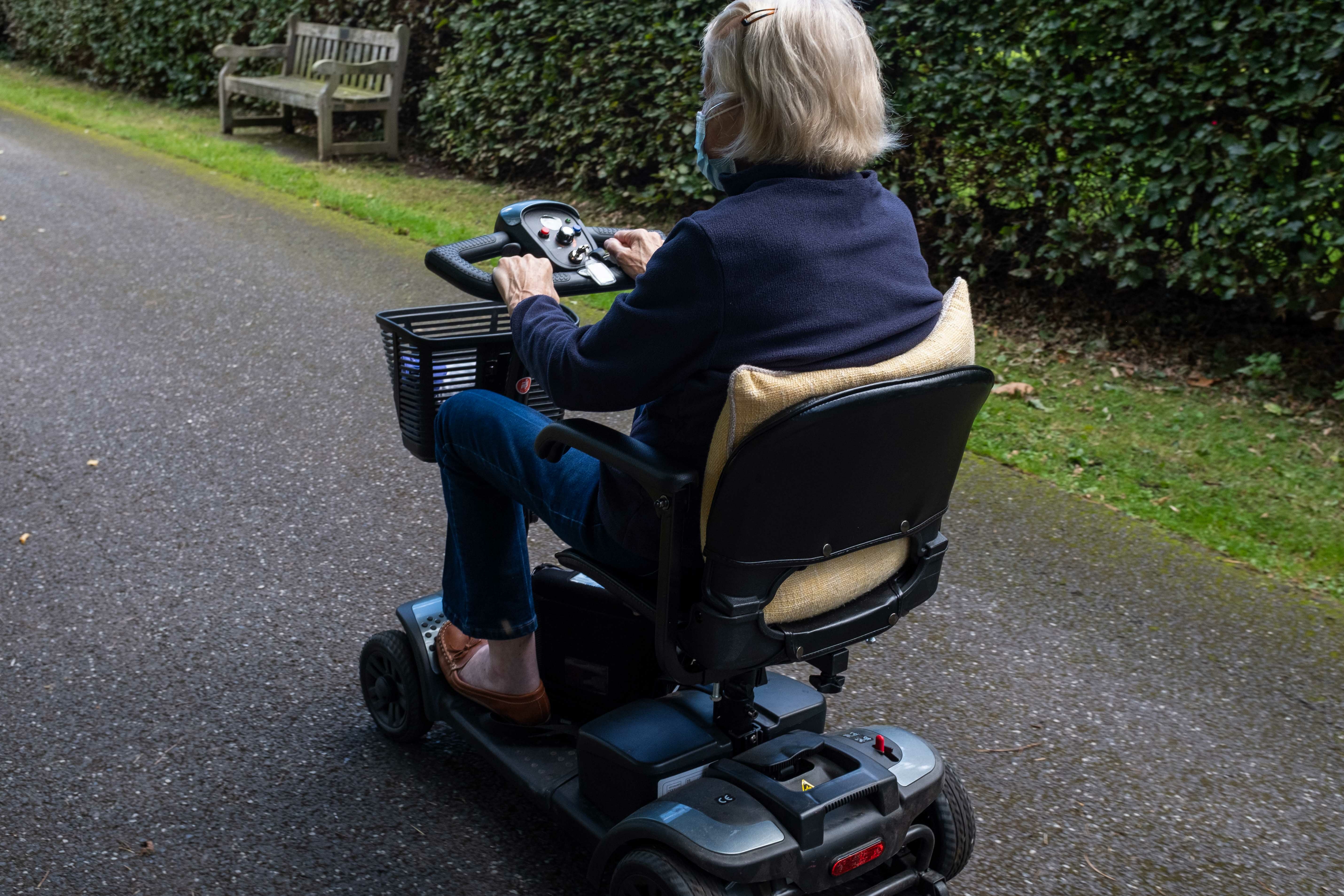 Elderly parent using a mobility scooter outdoors on a paved path – mobility scooters offer elderly parents greater independence and comfort when travelling short distances outside the home.