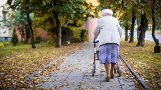 Older adult walking outdoors with a rollator walker – rollators provide elderly parents with stability, support, and a seat for resting during longer walks or trips outside the home.