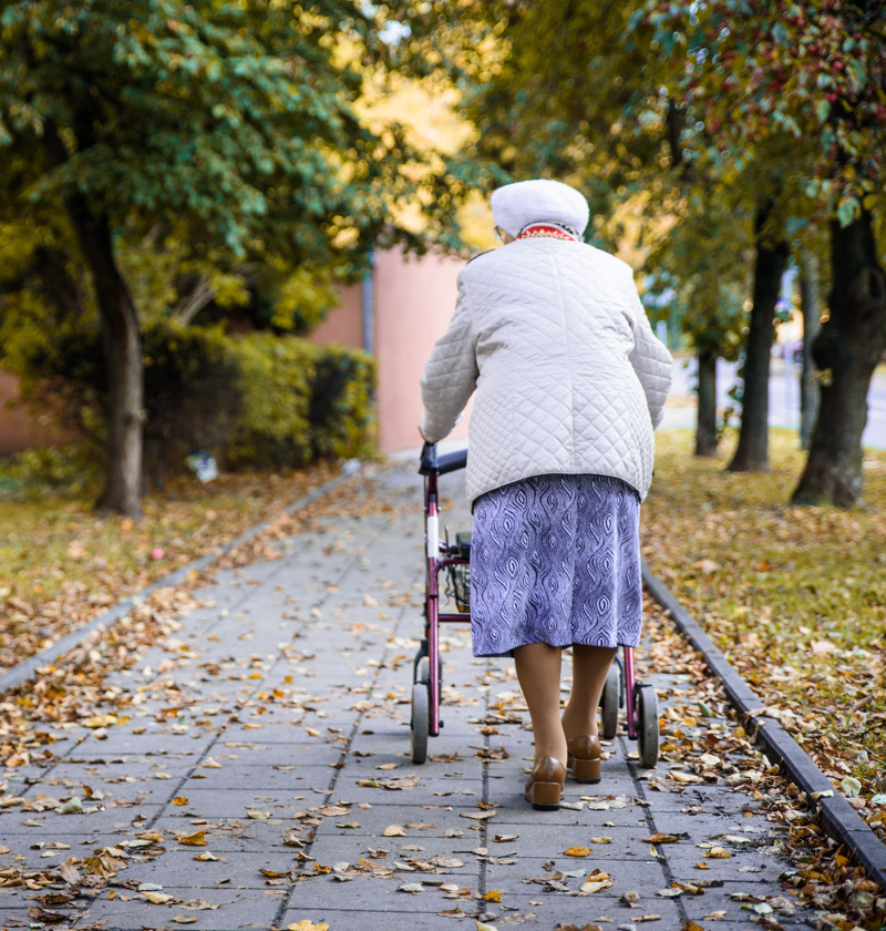 Older adult walking outdoors with a rollator walker – rollators provide elderly parents with stability, support, and a seat for resting during longer walks or trips outside the home.