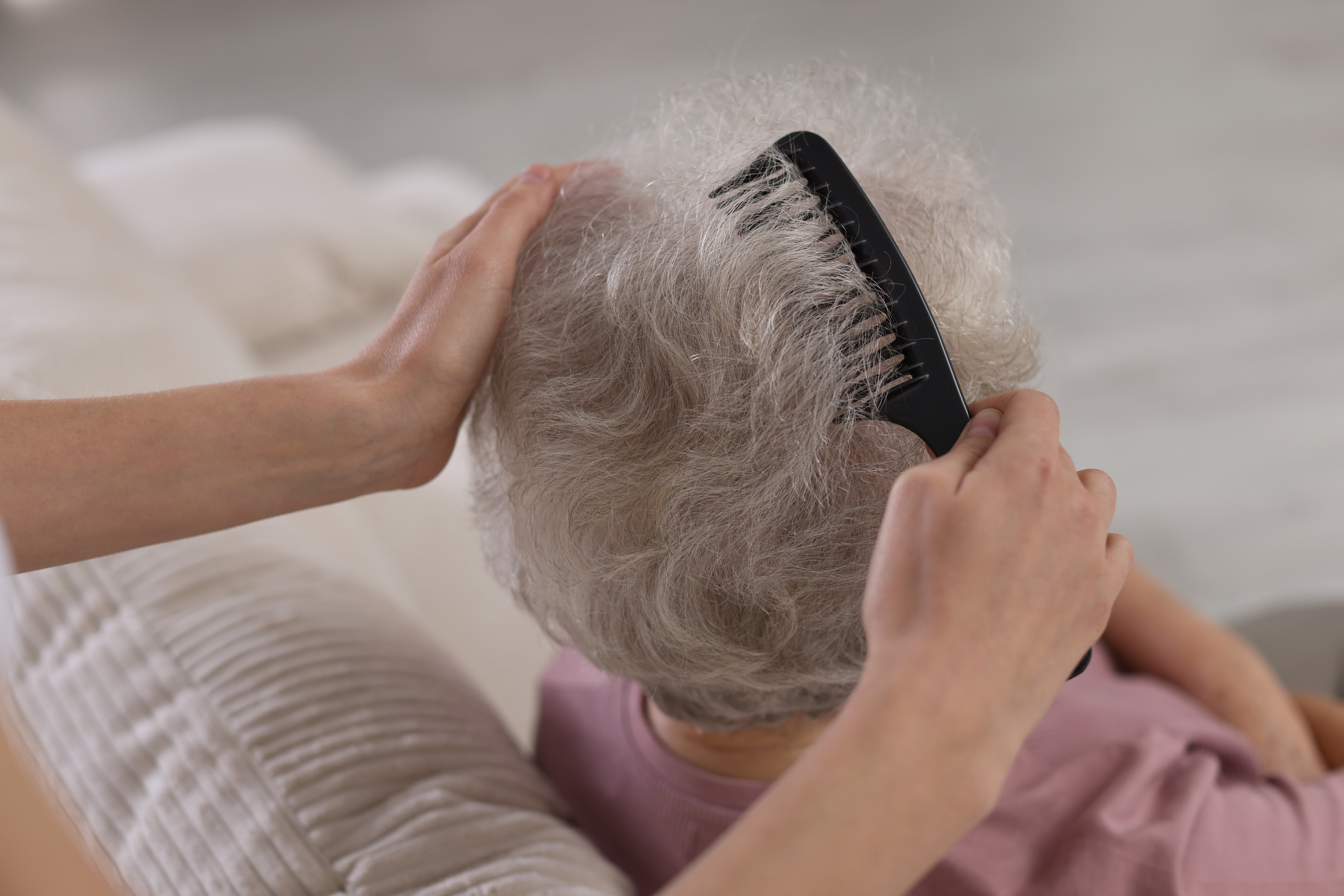 Carer gently combing an older adult’s hair – waterless hair products are a convenient option for elderly parents who have limited mobility or find regular hair washing difficult.