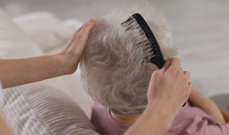 Carer gently combing an older adult’s hair – waterless hair products are a convenient option for elderly parents who have limited mobility or find regular hair washing difficult.