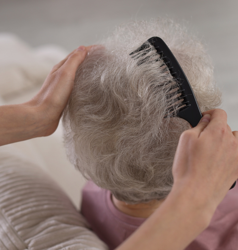 Carer gently combing an older adult’s hair – waterless hair products are a convenient option for elderly parents who have limited mobility or find regular hair washing difficult.