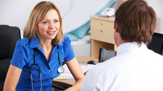 Consulting a GP About Elderly Parent’s Health – A female doctor in a blue uniform listens attentively to a patient. A reminder of the importance of regular check-ups and seeking professional medical advice for elderly loved ones.