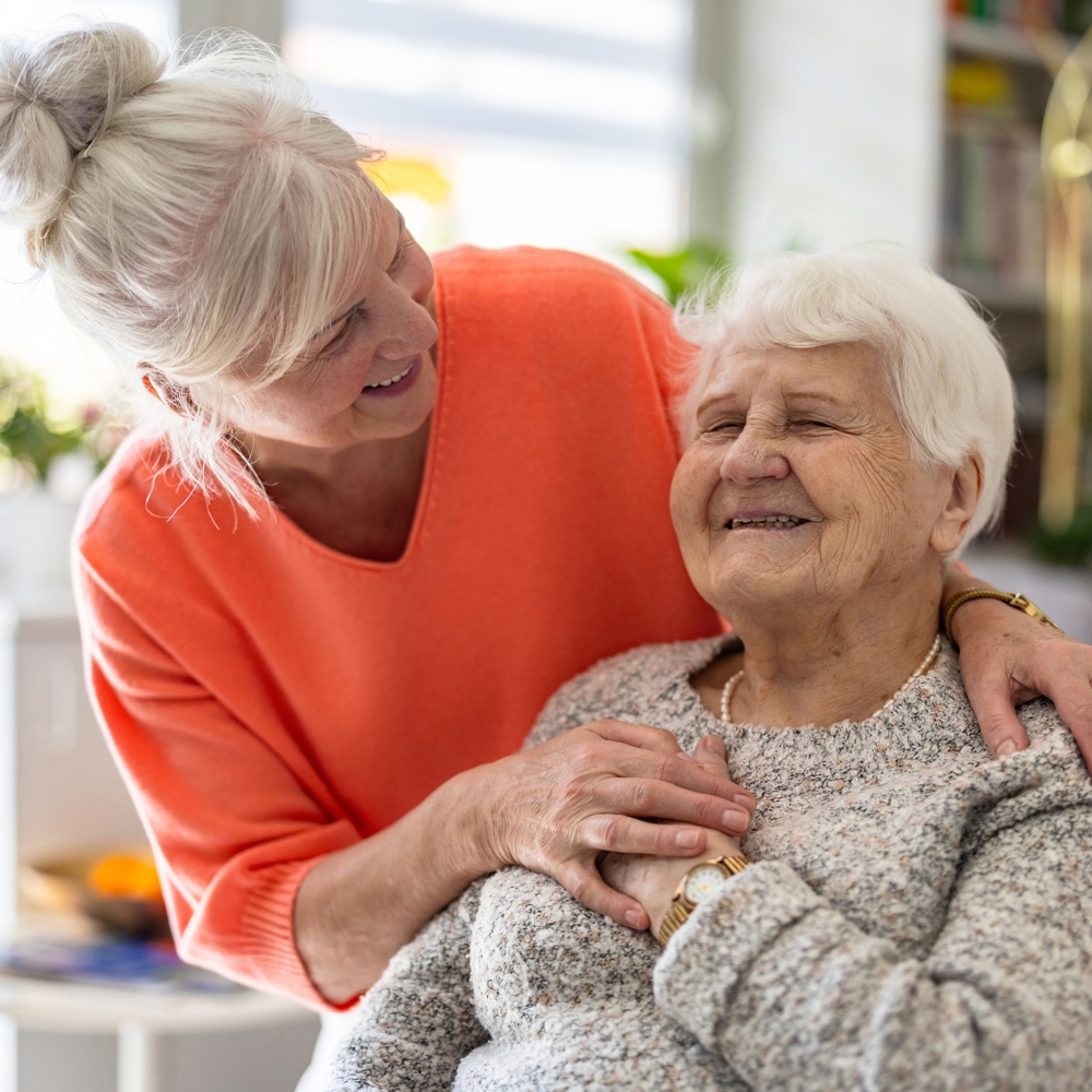 Woman in orange jumper hugging older woman, both smiling