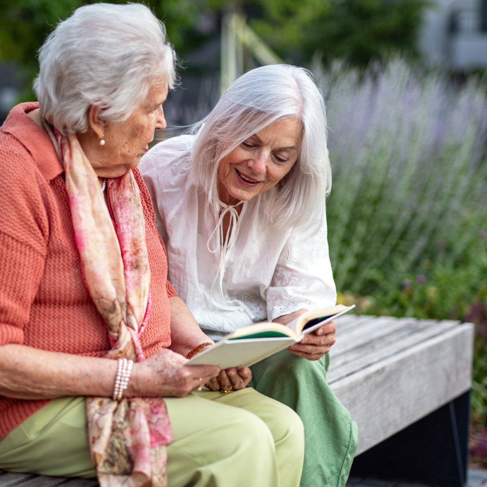 Carent and parent sitting on a bench outside and looking at a book