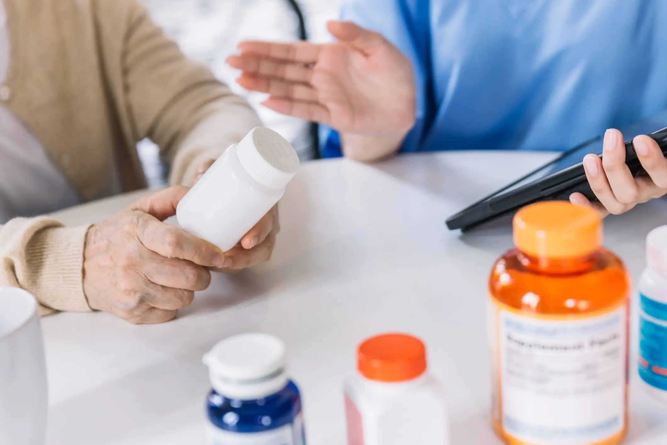 Older person holding a bottle of pills, with many other containers of pills around 