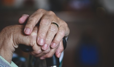 Elderly hands crossed over a walking cane.