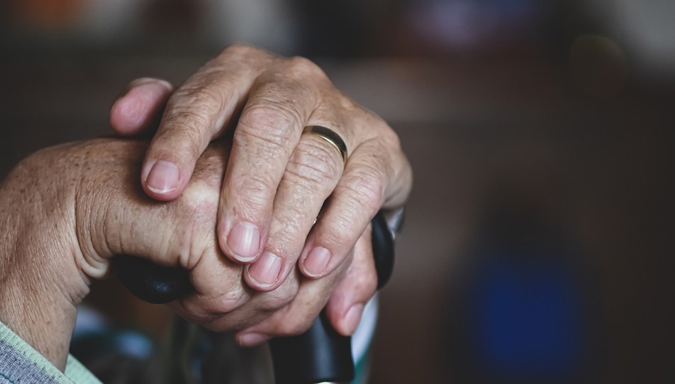Elderly hands crossed over a walking cane.