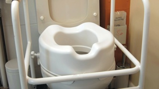 Toilet fitted with a raised seat and support frame – toilet seat risers help elderly parents with limited mobility sit and stand more easily, reducing strain and supporting safer bathroom use.