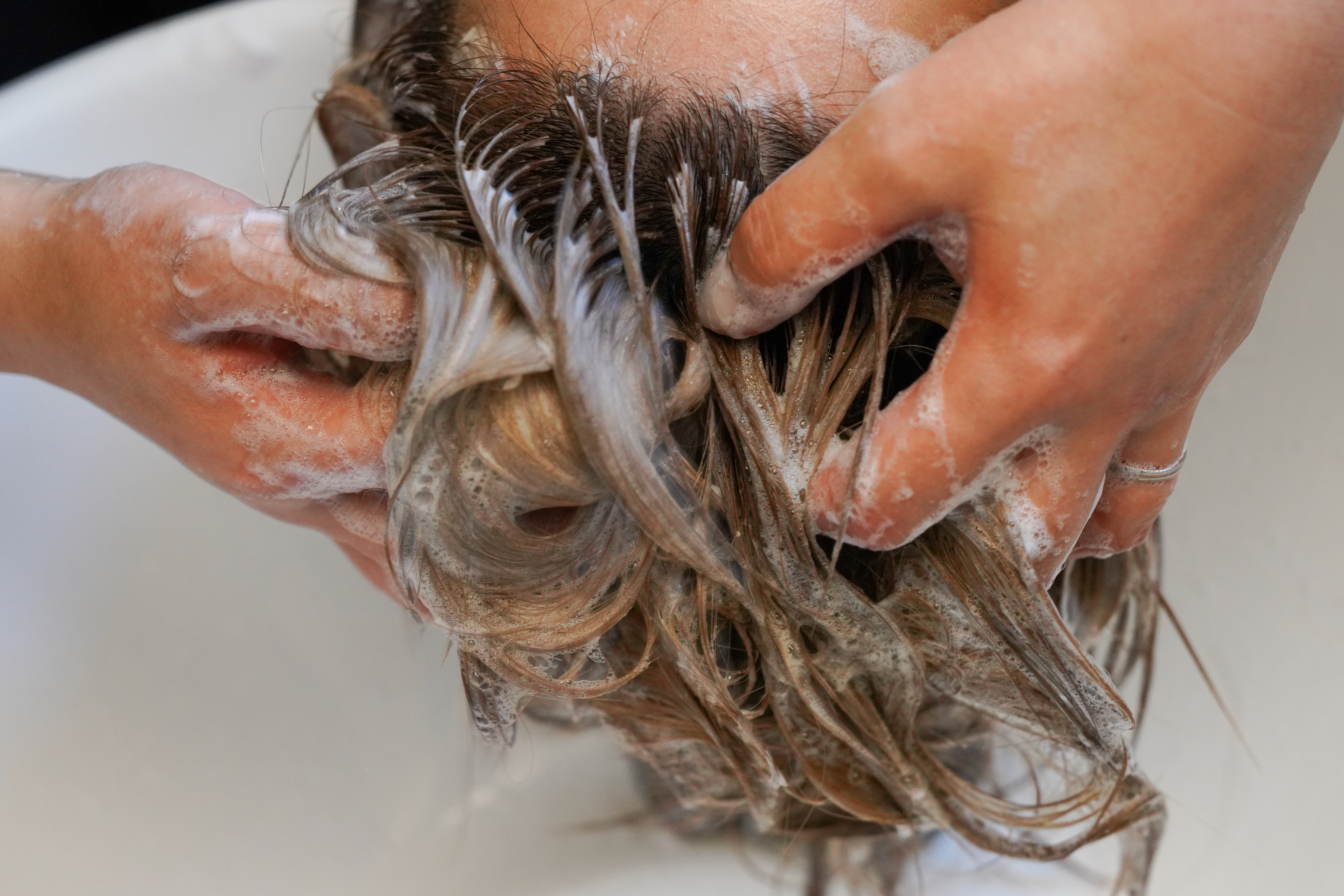 Carer washing an older adult’s hair over a basin – hair washing trays make it easier to wash hair for elderly parents with limited mobility, reducing the need to bend or move to a shower.