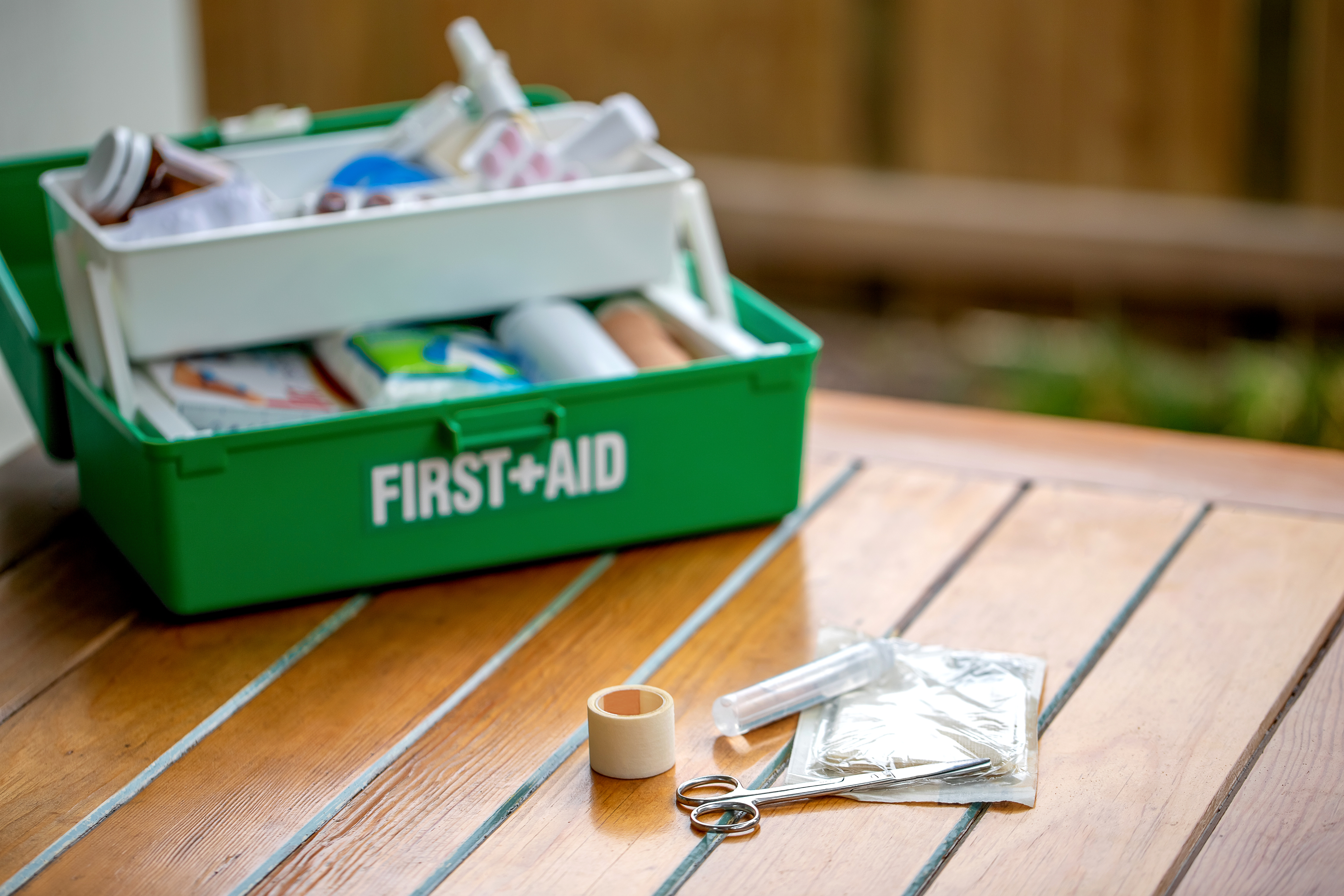 Fully stocked green first aid kit open on a table, with medical supplies including scissors, bandages, tape, and antiseptic wipes – essential home safety item for carers looking after elderly parents.
