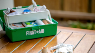 Fully stocked green first aid kit open on a table, with medical supplies including scissors, bandages, tape, and antiseptic wipes – essential home safety item for carers looking after elderly parents.