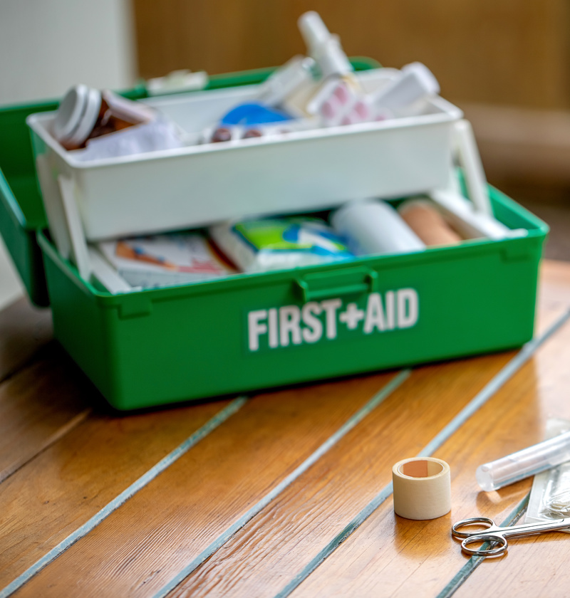 Fully stocked green first aid kit open on a table, with medical supplies including scissors, bandages, tape, and antiseptic wipes – essential home safety item for carers looking after elderly parents.