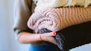 A woman carrying blankets of three shades of colours - white, pink and navy