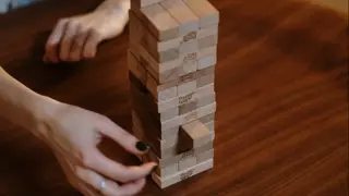 Wooden Jenga blocks with a middle aged woman taking out a piece