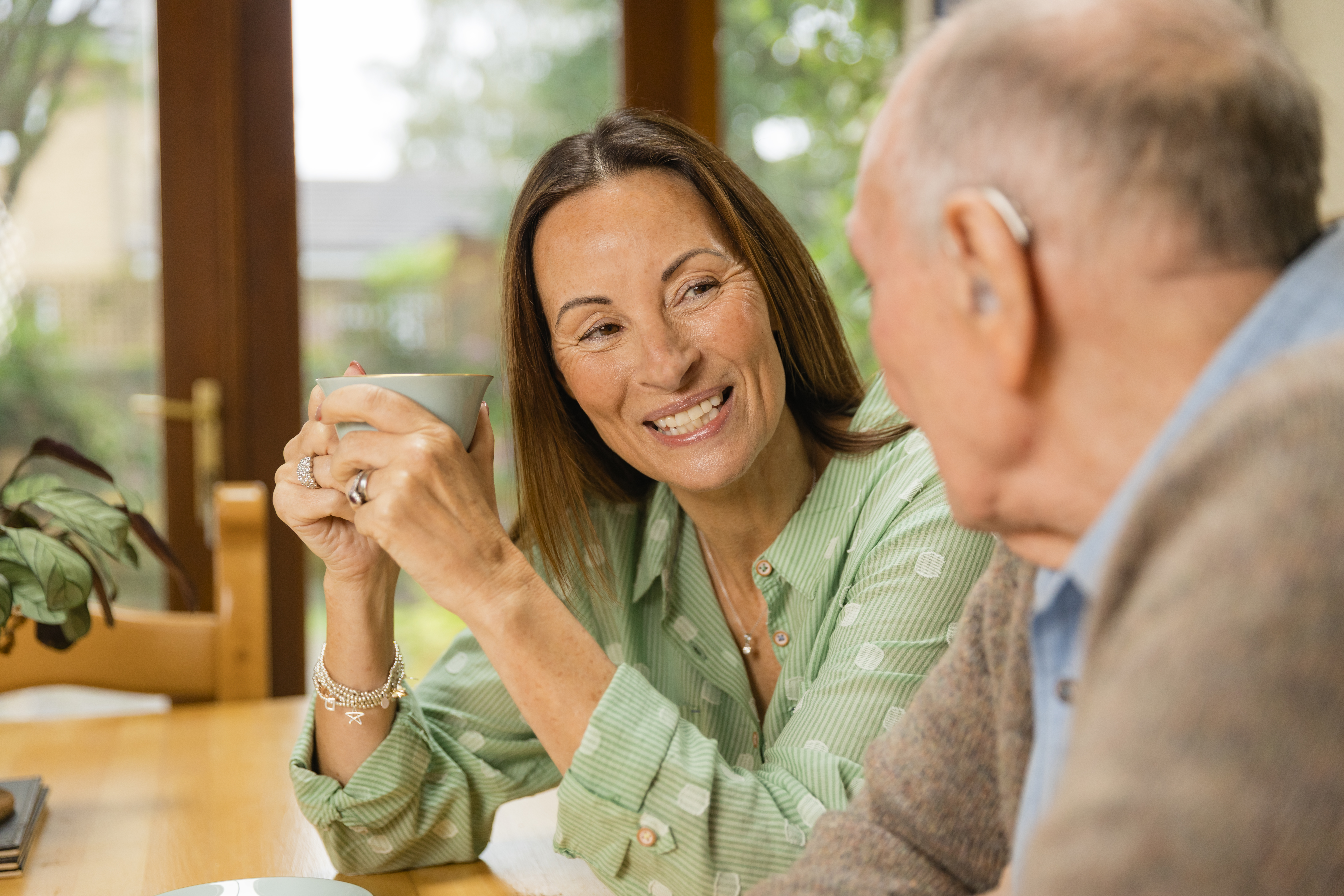 A woman sitting at a table having a cup of tea with her elderly parent. 