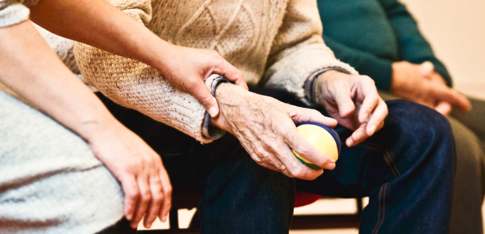 An elderly person holding a ball and being helped by a carent 