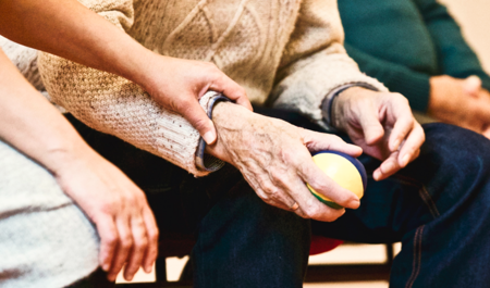 An elderly person holding a ball and being helped by a carent 