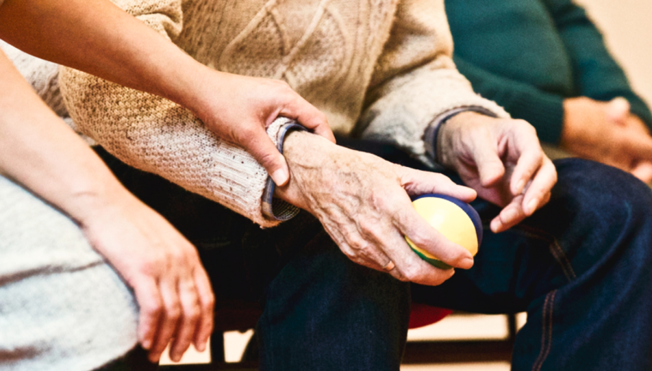 An elderly person holding a ball and being helped by a carent 