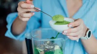 A woman putting green powder into a smoothie machine