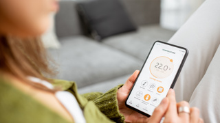 Someone reading their thermostat on their phone. Smart heating system. Representing heating, energy awareness, bills and PSR entitlement for your elderly parent.