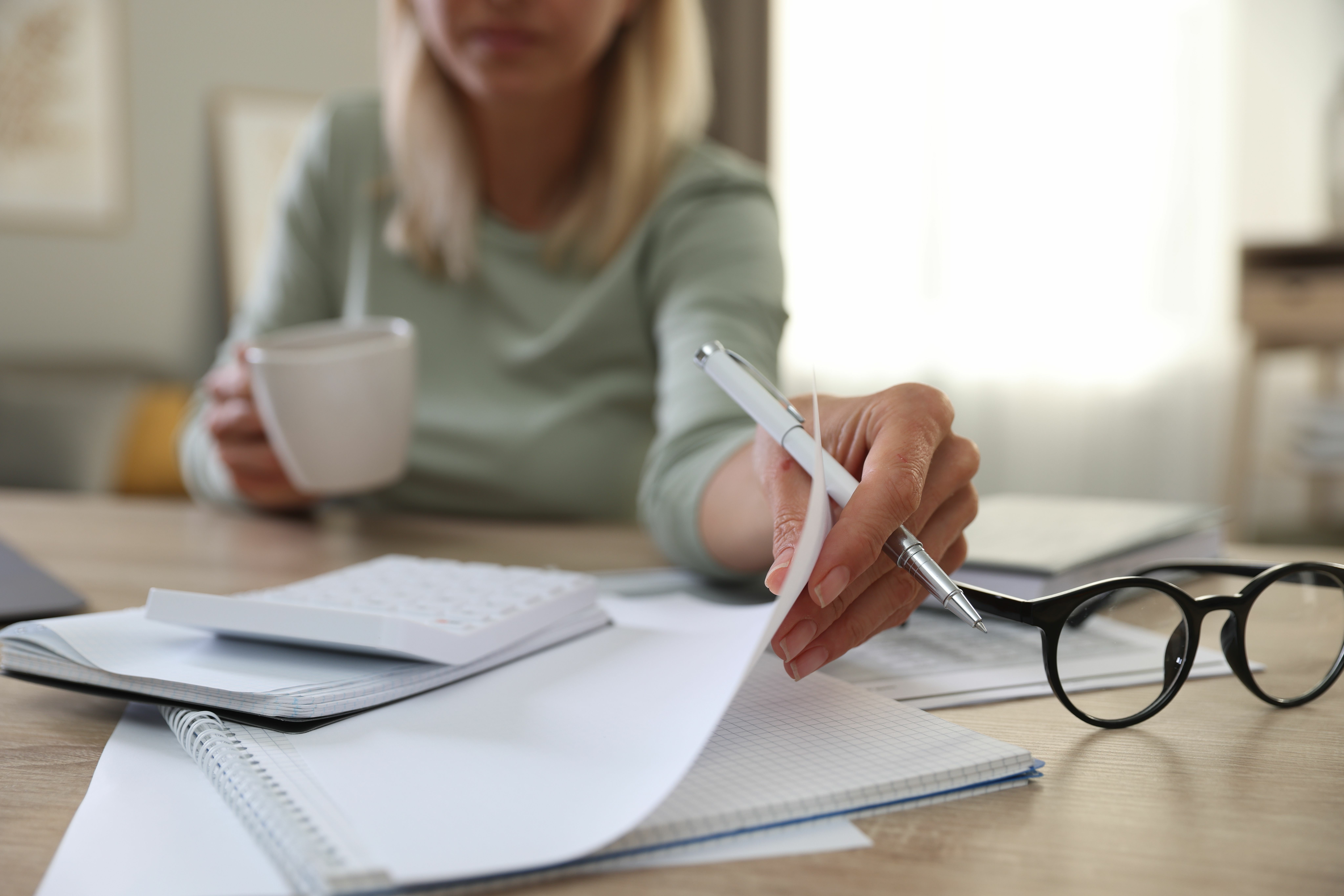 Managing Household Finances for Elderly Care – A woman reviews financial documents while holding a coffee cup, symbolising the responsibility of managing bills, care costs, and financial planning for ageing parents.