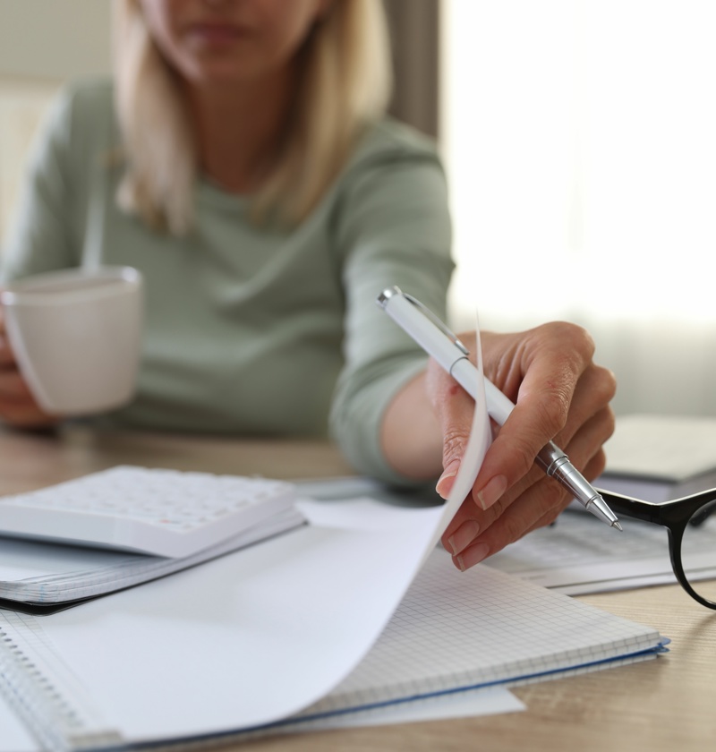 Managing Household Finances for Elderly Care – A woman reviews financial documents while holding a coffee cup, symbolising the responsibility of managing bills, care costs, and financial planning for ageing parents.