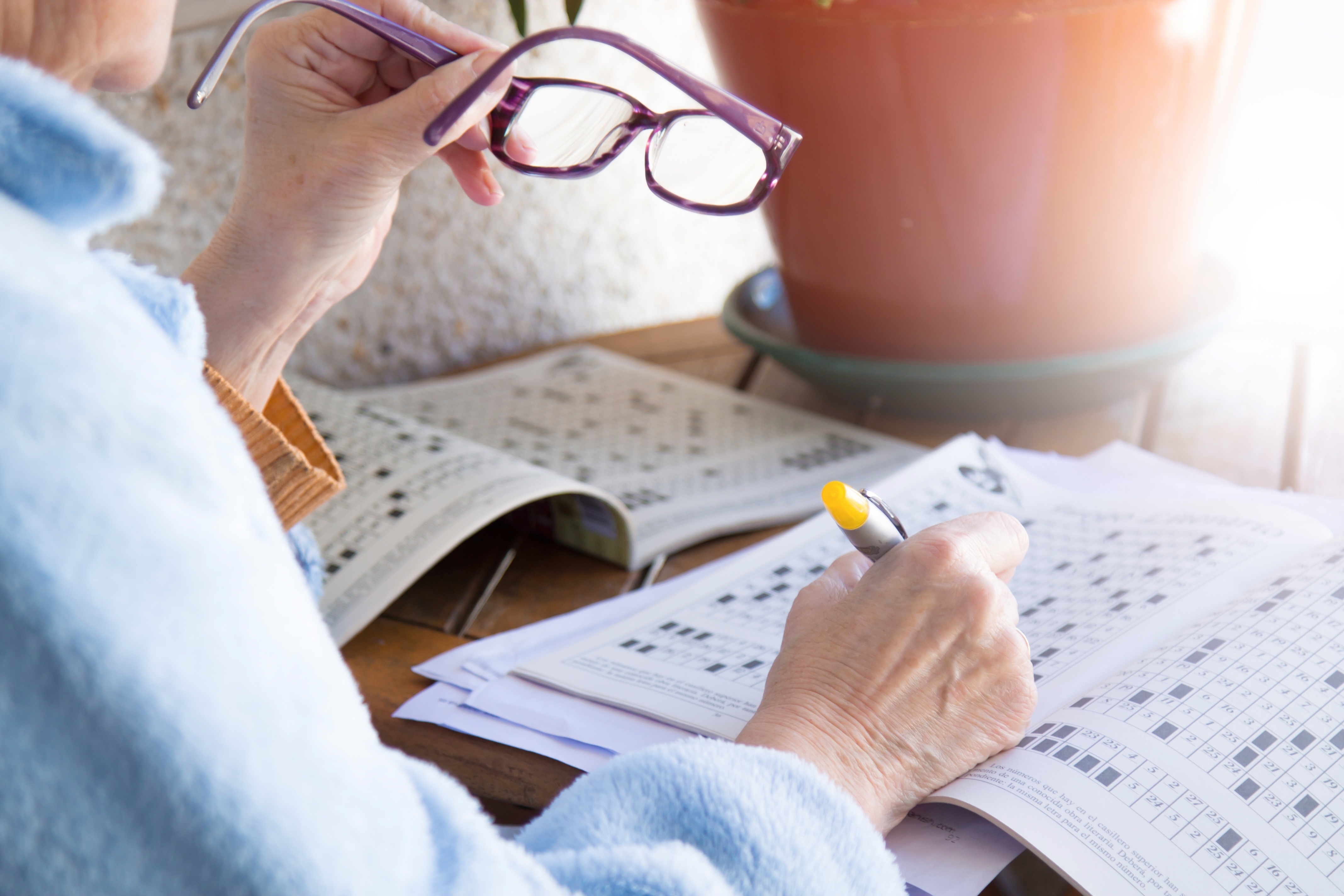 Older adult holding reading glasses while completing a puzzle in a dementia activity book – these books support memory, focus, and enjoyment for elderly parents living with cognitive decline.