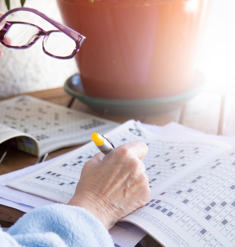 Older adult holding reading glasses while completing a puzzle in a dementia activity book – these books support memory, focus, and enjoyment for elderly parents living with cognitive decline.