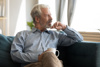 Finding Moments to reflect on your Emotions as a Carent – A silver-haired man sits on a plush sofa, holding a coffee cup while staring thoughtfully into the distance. A representation of taking time for oneself amidst the responsibilities of supporting an ageing parent.