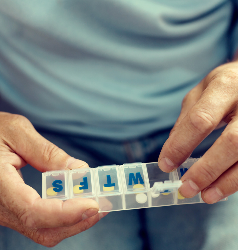 Weekly pill dispenser for elderly parents – older adult using a daily pill organiser with labelled compartments to manage medication safely and independently at home.