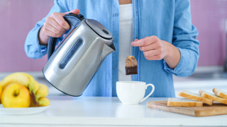Person making tea with a stainless steel electric kettle – suitable for elderly parents with features like an easy-grip handle, wide spout, and clear water level for safer pouring.