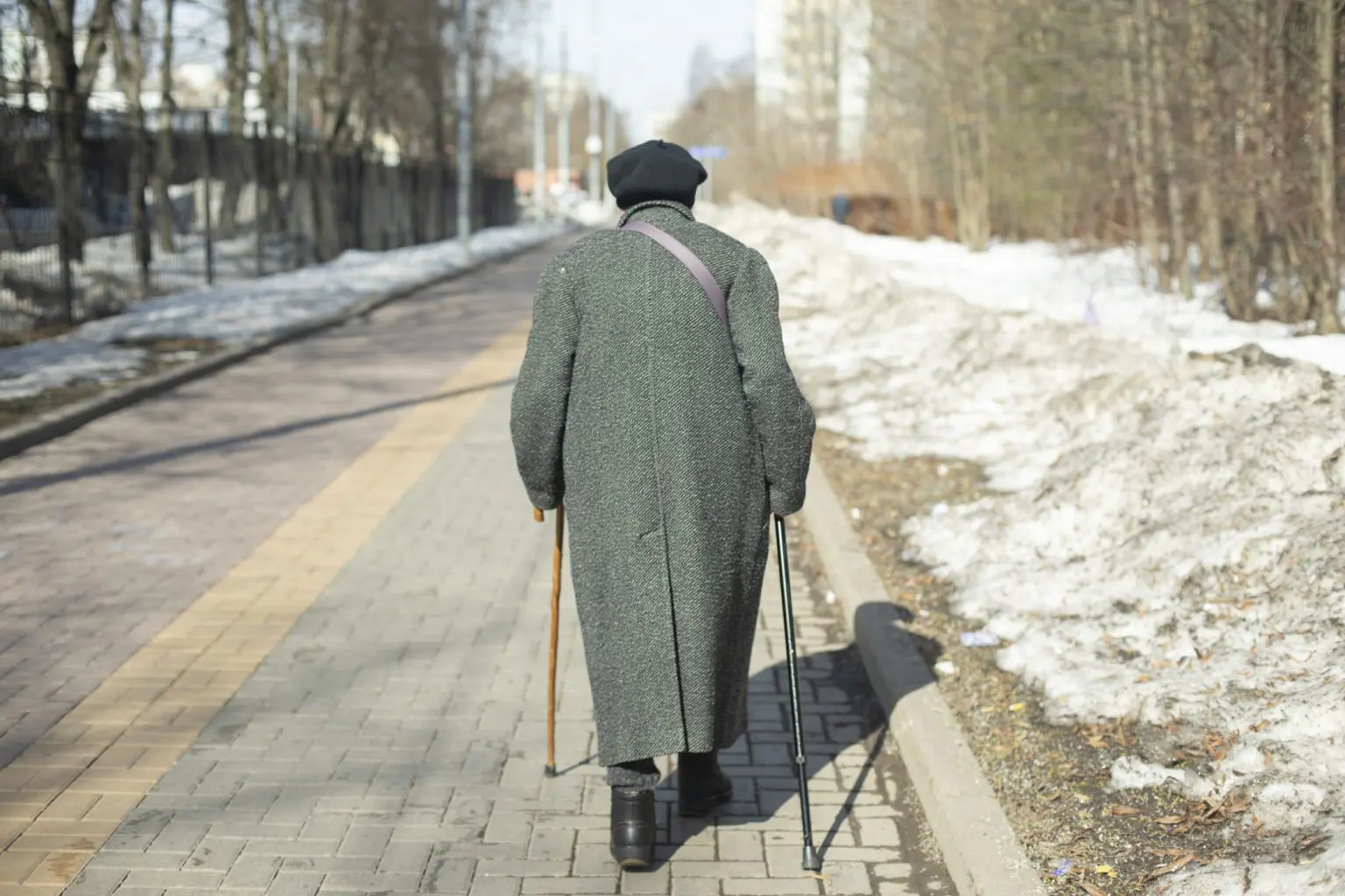 Woman walking with 2 sticks in the cold. Used to represent solo walking by your elderly parent.
