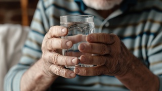 Older adult holding a glass with both hands – highlighting the importance of non-spill cups for elderly parents with limited grip strength, arthritis, or hand tremors to reduce spills and support safe hydration.